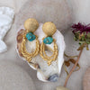 Golden pilgrim's earrings displayed on an oyster shell with flower. Made by Jesse Ball at Jupiter's Grace